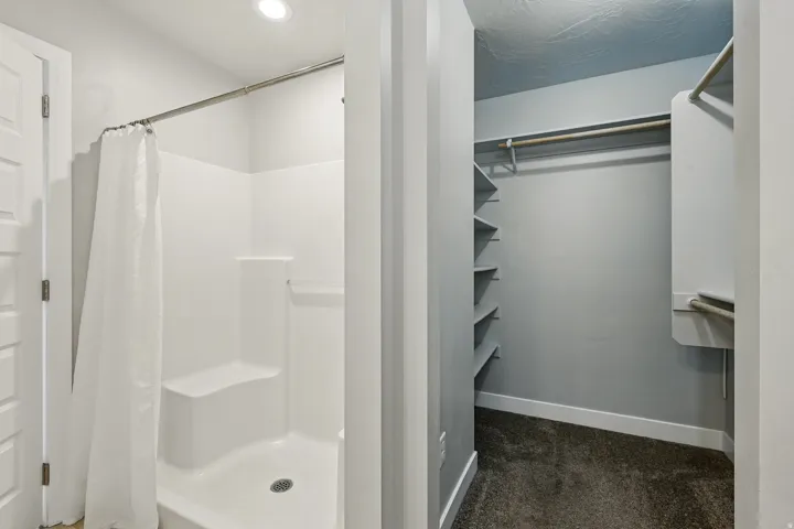 Bathroom featuring a walk in closet, a stall shower, and dark colored carpet