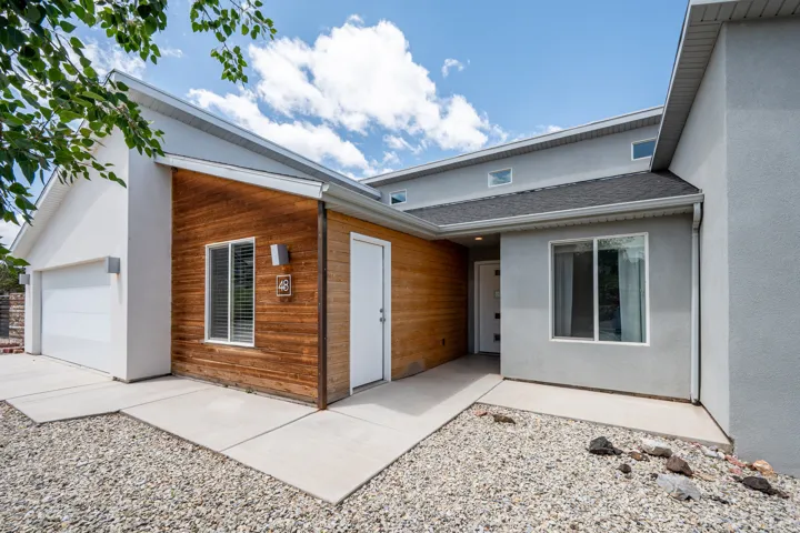 View of exterior entry with a shingled roof, stucco siding, and an attached garage