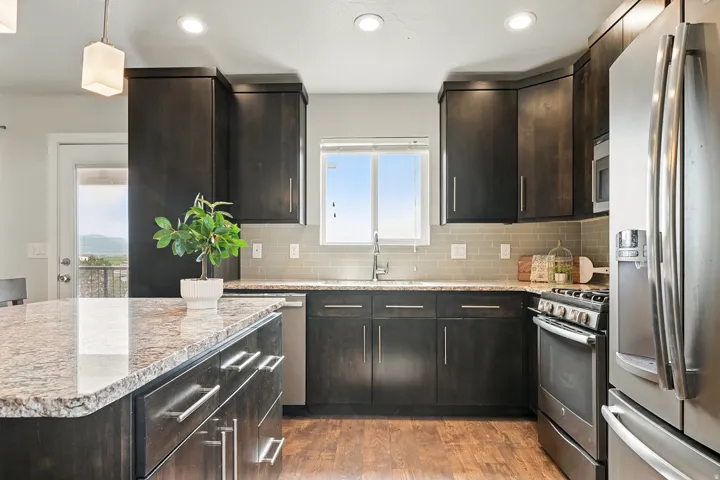 Kitchen with stainless steel appliances, hanging light fixtures, light stone countertops, dark brown cabinetry, and recessed lighting