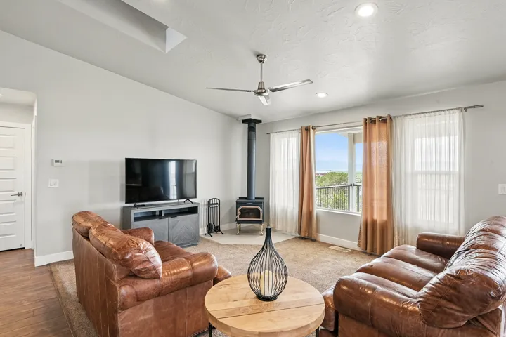 Living area featuring a wood stove, recessed lighting, a ceiling fan, vaulted ceiling, and a skylight