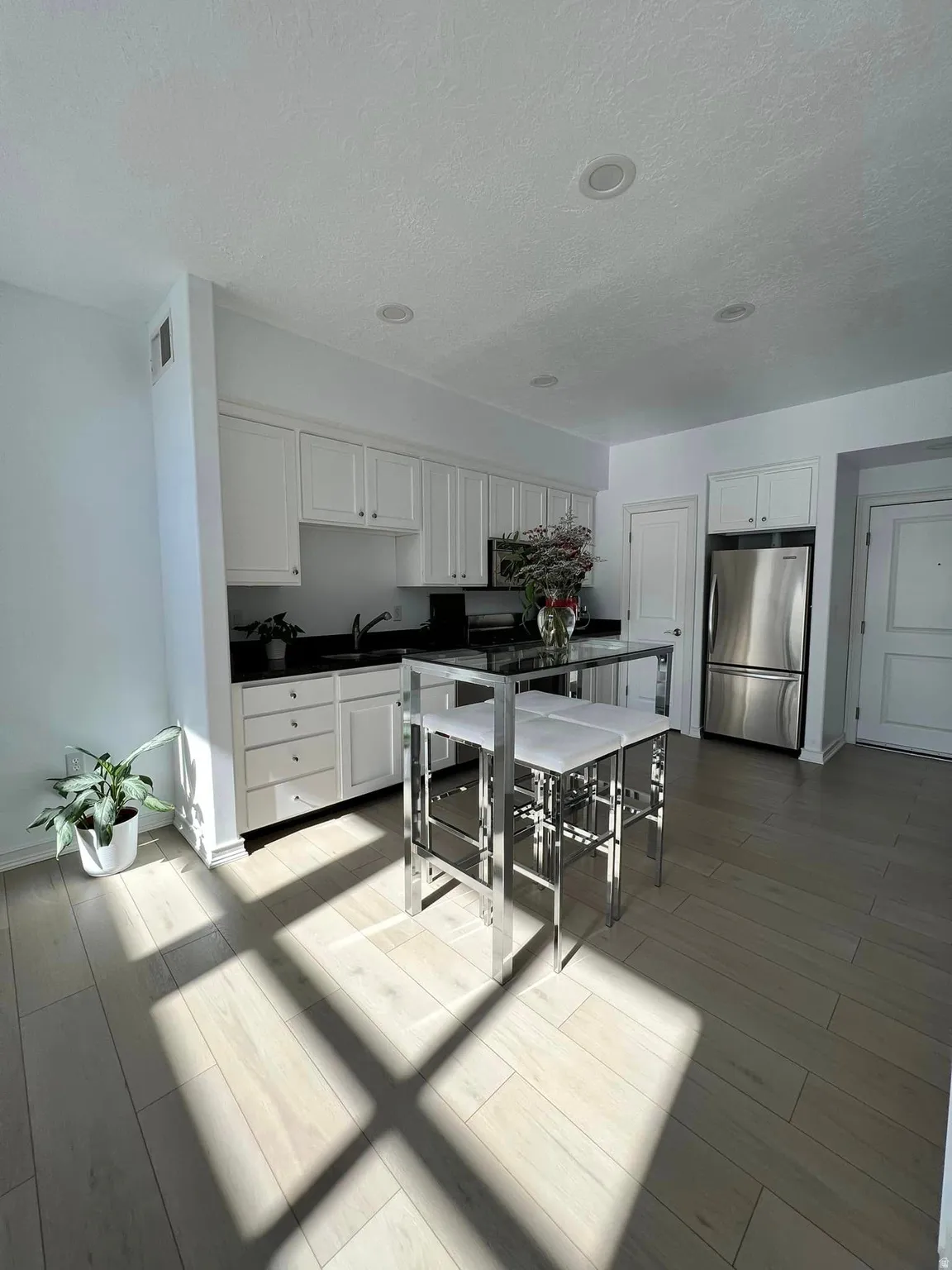 Kitchen featuring white cabinets, freestanding refrigerator, dark countertops, a textured ceiling, and wood finish floors