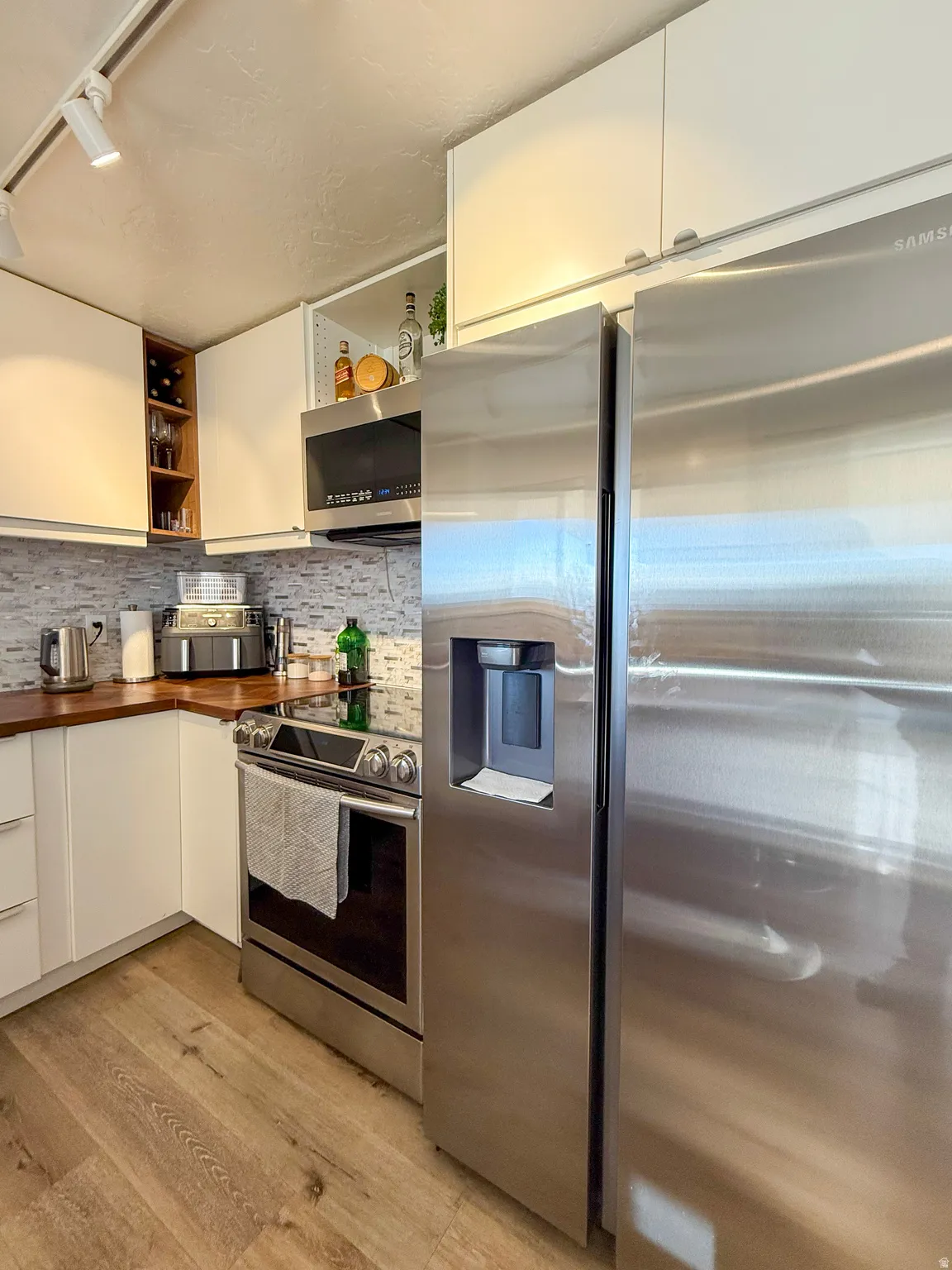 Kitchen featuring rail lighting, stainless steel appliances, white cabinetry, and open shelves