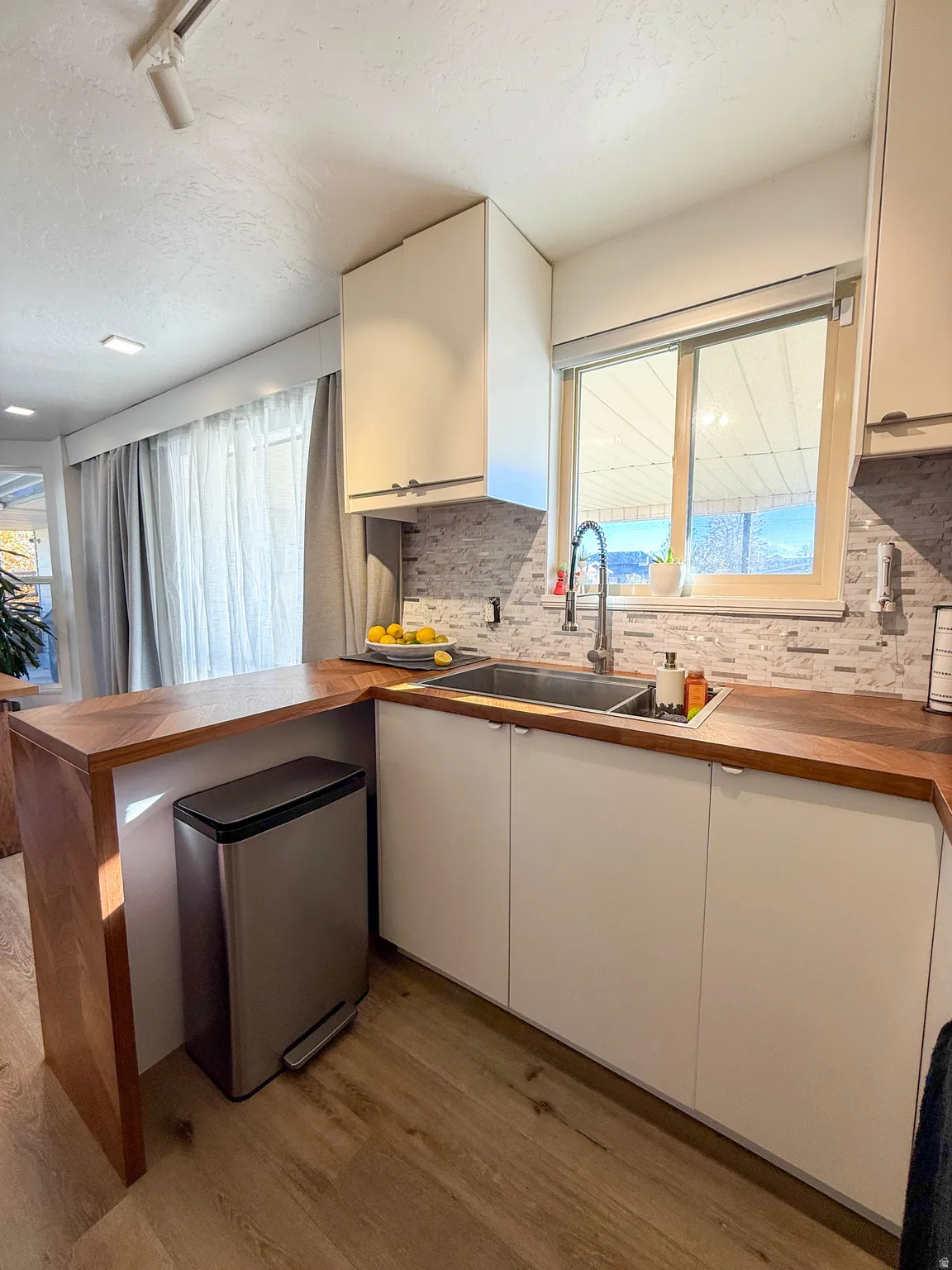 Kitchen featuring a peninsula, butcher block countertops, light wood-type flooring, white cabinets, and decorative backsplash