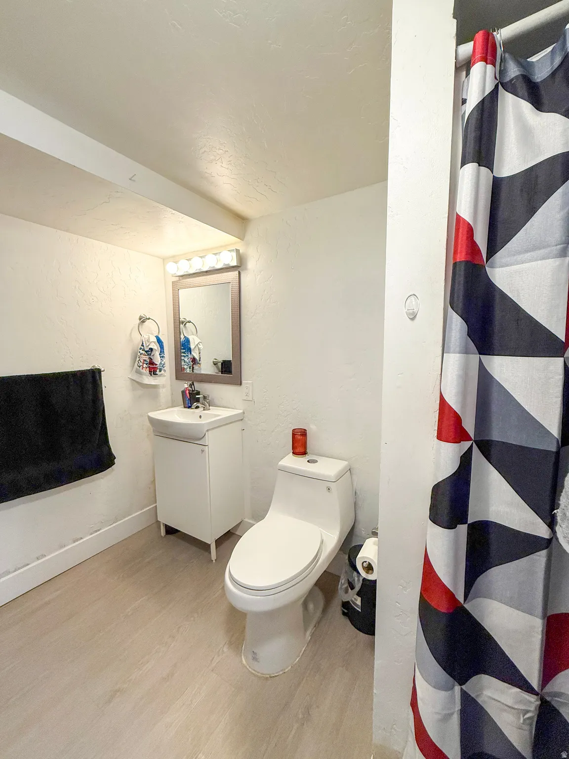 Bathroom featuring a textured wall, a shower with shower curtain, light wood-style flooring, vanity, and a textured ceiling