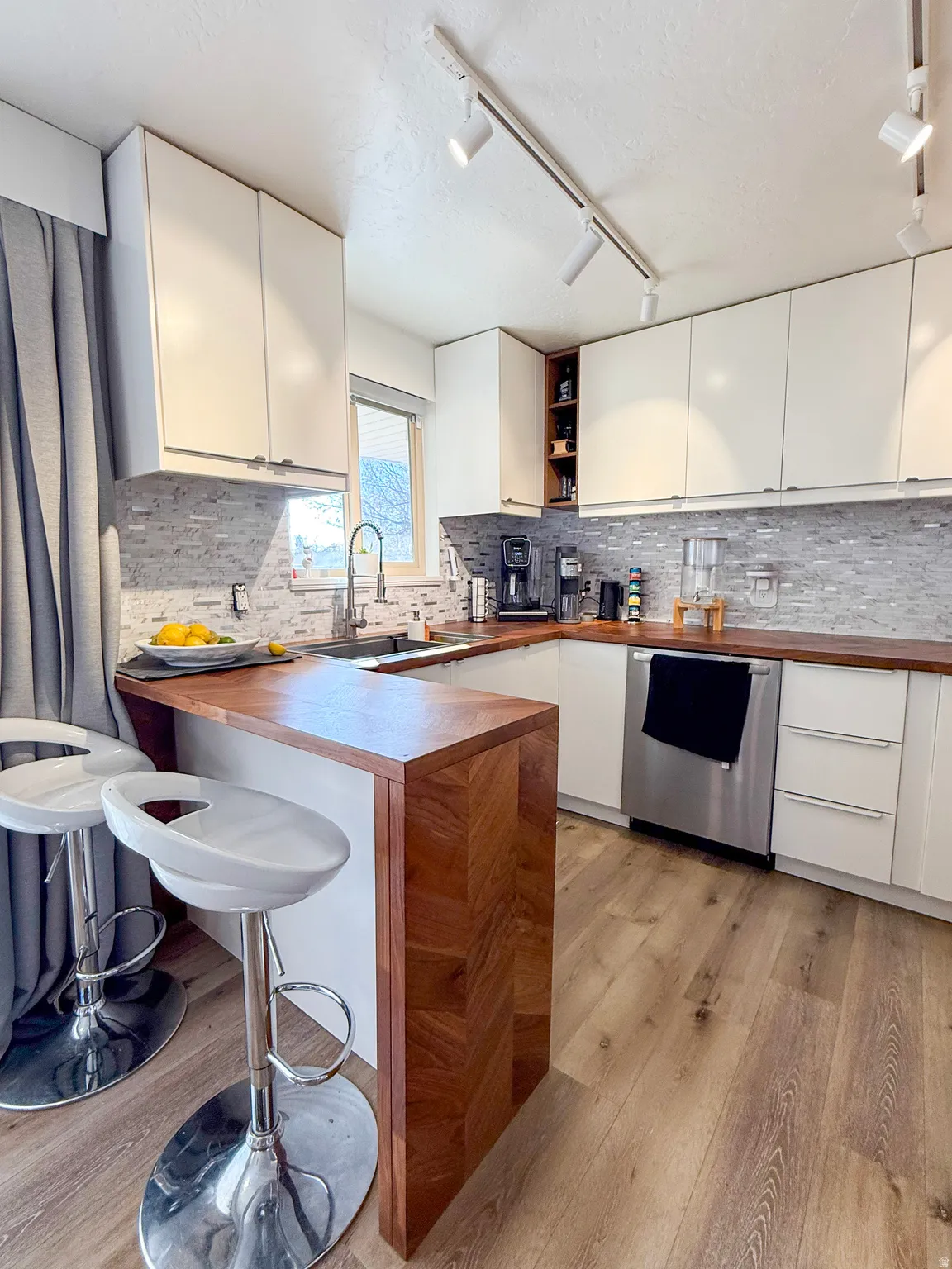 Kitchen featuring rail lighting, a peninsula, a breakfast bar, white cabinetry, and a textured ceiling