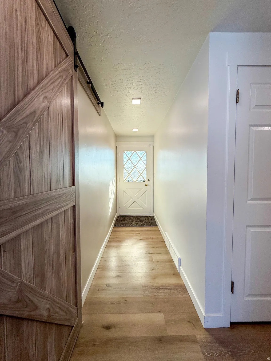 Hall with a barn door, light wood-style floors, and a textured ceiling