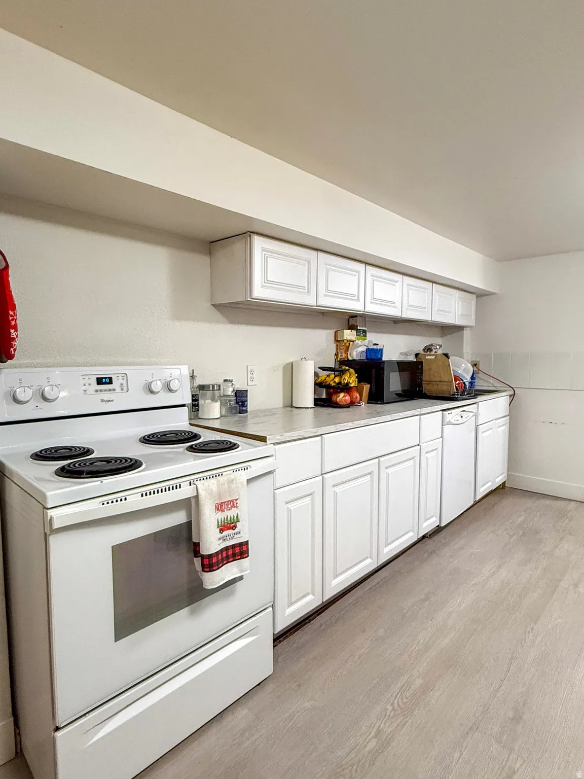 Kitchen featuring white appliances, white cabinets, light countertops, and light wood-type flooring