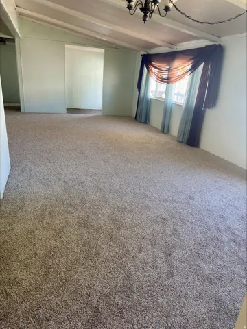 Spacious room featuring vaulted ceilings with exposed beams, broadloom carpeting, and a window with natural light