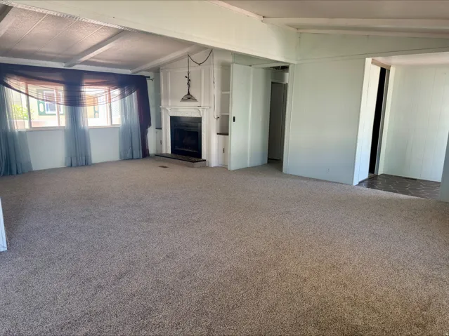 Spacious living area featuring wall-to-wall carpeting, a white painted fireplace with a dark surround, and an integrated built-in shelf