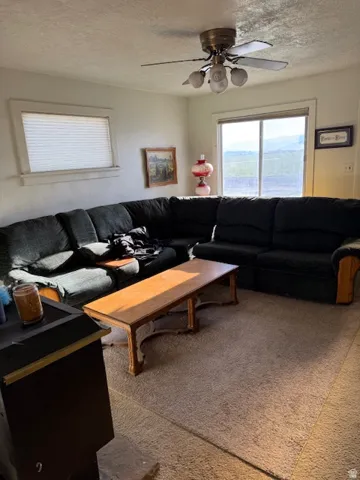 Living room with a textured ceiling, carpet floors, and ceiling fan