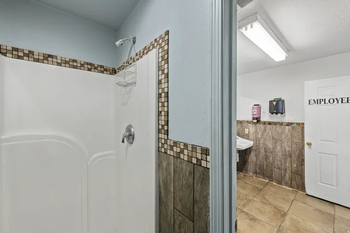 Bathroom with tile walls, wainscoting, a shower, a textured ceiling, and tile patterned flooring