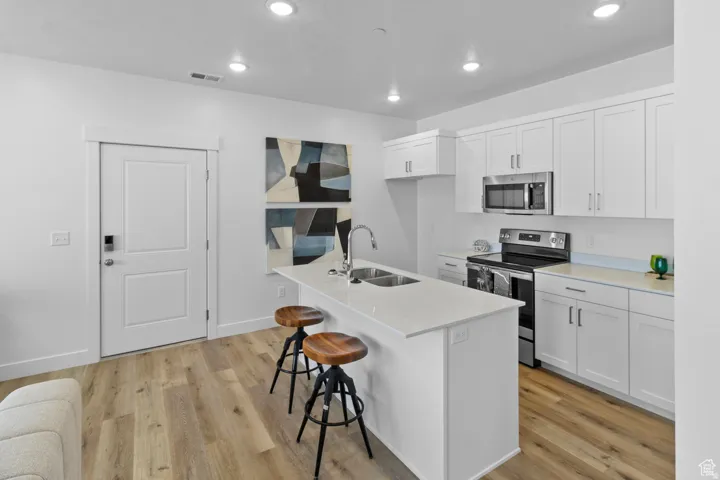 Kitchen featuring appliances with stainless steel finishes, white cabinetry, a breakfast bar area, an island with sink, and recessed lighting