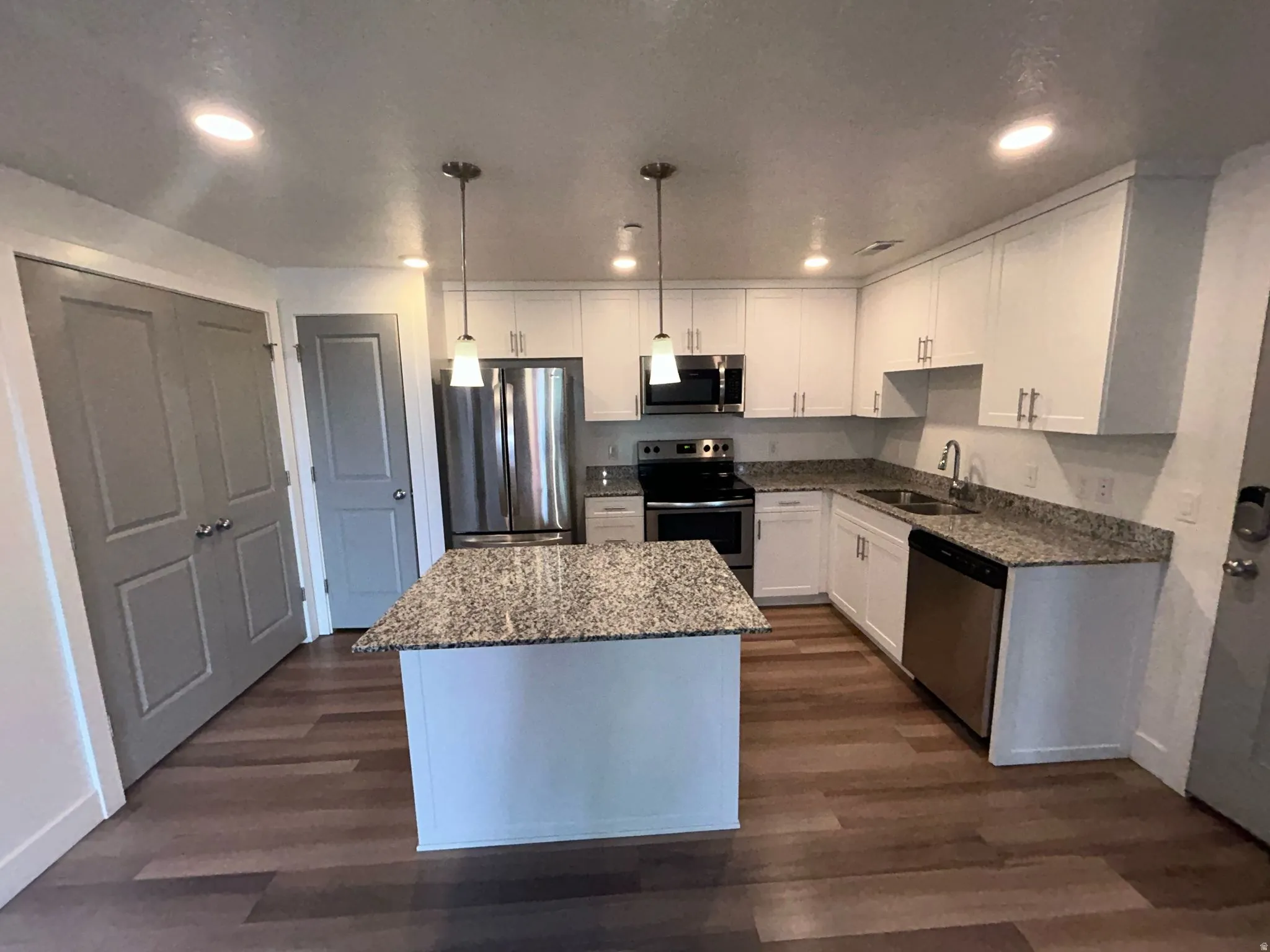 Kitchen with appliances with stainless steel finishes, white cabinetry, dark stone counters, a kitchen island, and recessed lighting