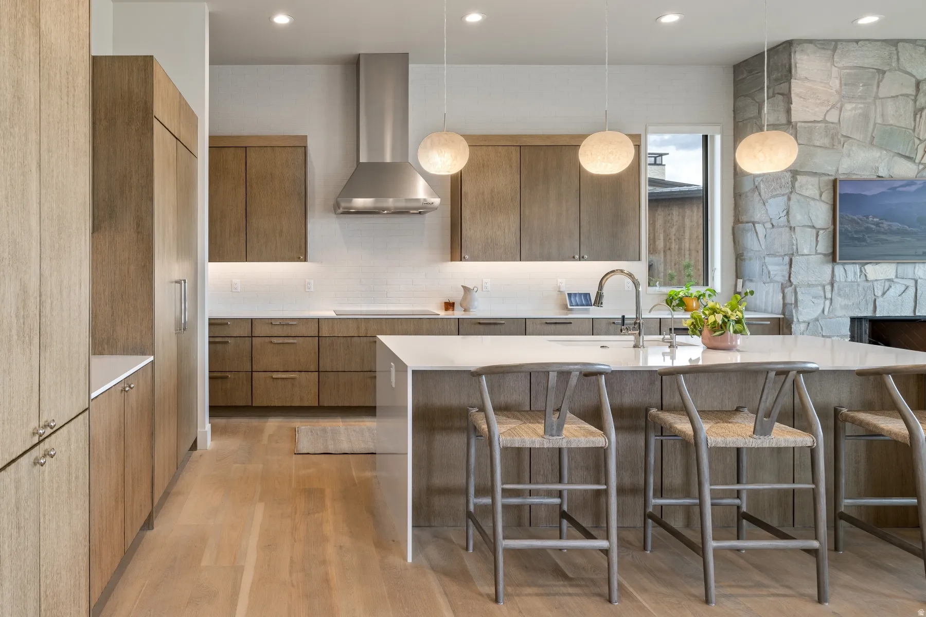 Kitchen featuring modern cabinets, hanging light fixtures, wall chimney range hood, light stone counters, and light wood-style floors