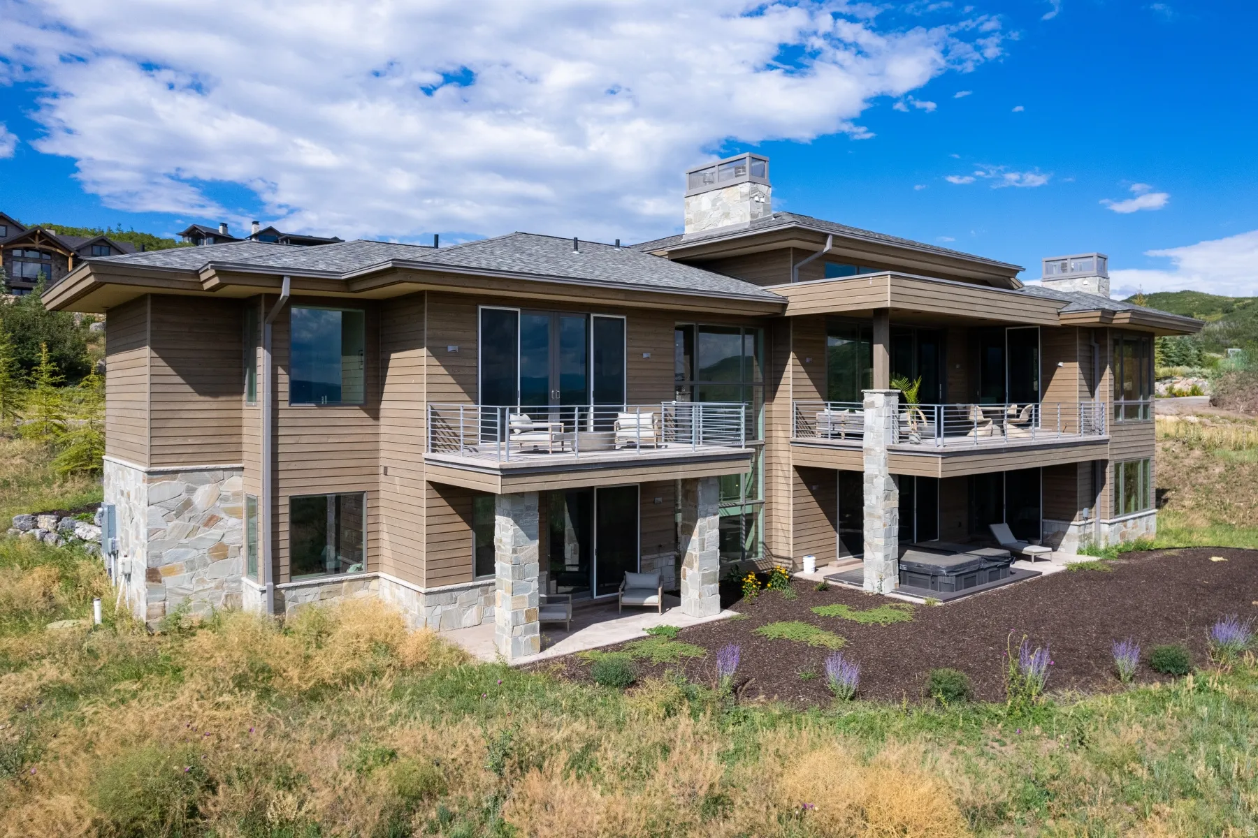 Rear view of property featuring a patio area, a chimney, stone siding, and a balcony