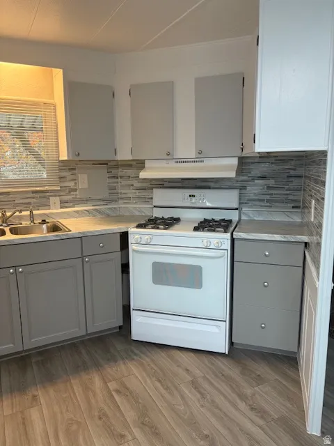 Kitchen featuring gray cabinets, white gas range oven, light countertops, light wood finished floors, and backsplash