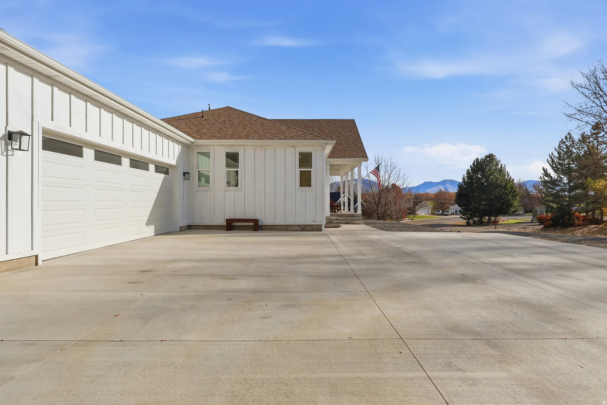 View of side of home featuring board and batten siding, driveway, roof with shingles, a garage, and a mountain view