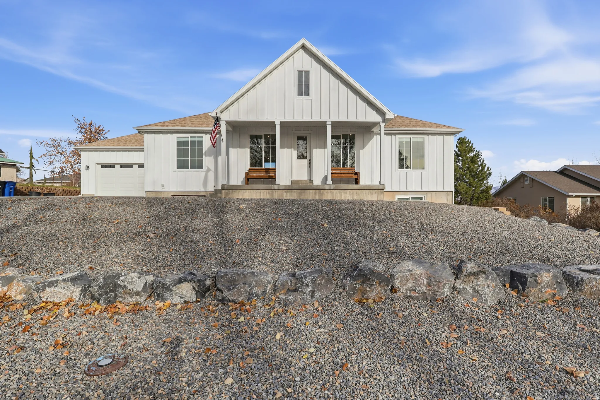 Modern inspired farmhouse featuring board and batten siding, a shingled roof, a porch, an attached garage, and gravel driveway