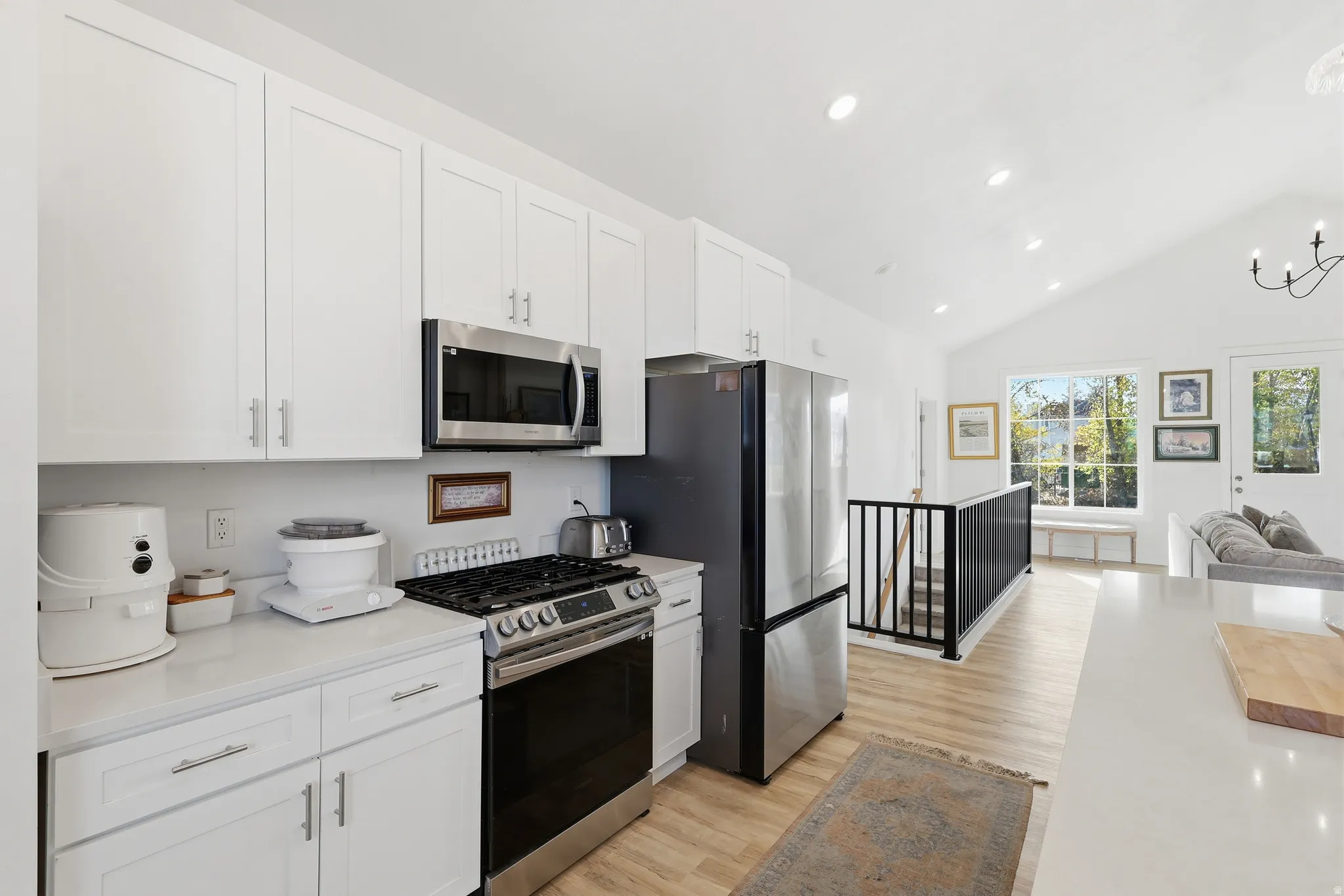 Kitchen with appliances with stainless steel finishes, open floor plan, white cabinets, light wood-type flooring, and a chandelier