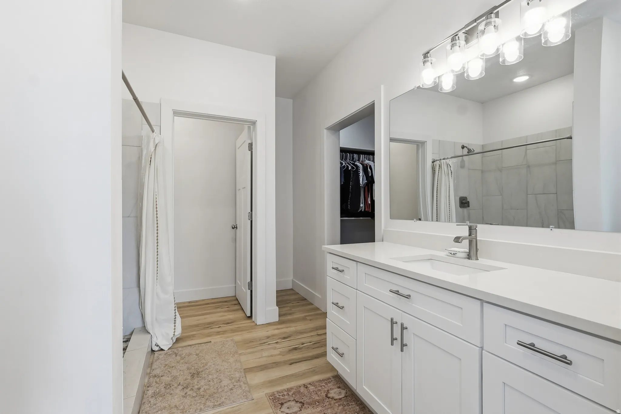 Full bath featuring vanity, a shower with curtain, light wood-style flooring, and a walk in closet