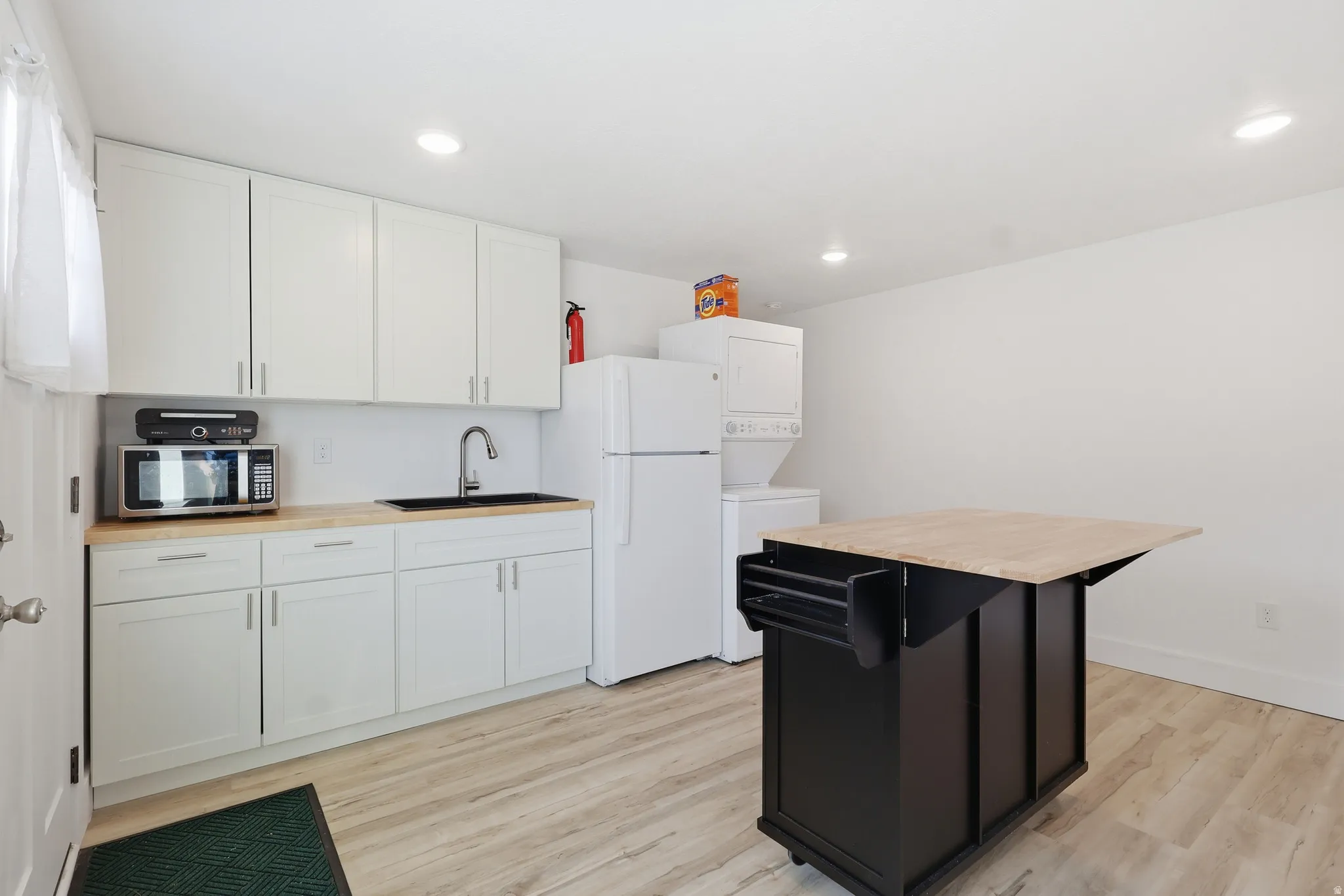 Kitchen with butcher block counters, freestanding refrigerator, stacked washer / dryer, white cabinets, and recessed lighting