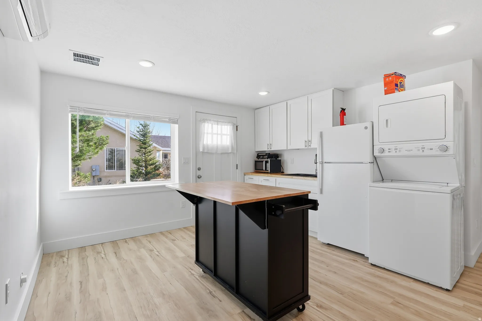 Kitchen featuring white cabinetry, a kitchen island, butcher block countertops, freestanding refrigerator, and an AC wall unit