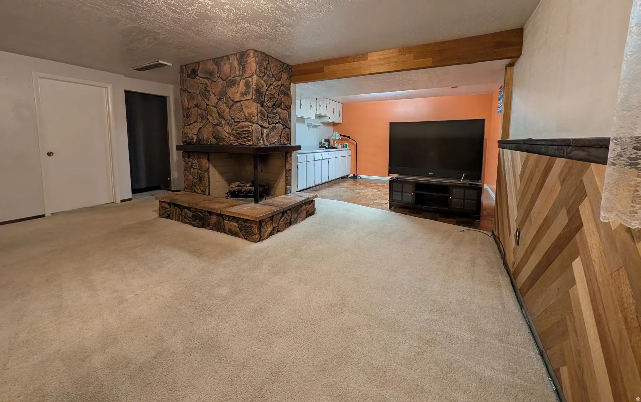 Living area featuring a stone-clad fireplace with a hearth, light-toned carpet, wood paneling with a diagonal pattern, and a wood beam ceiling accent