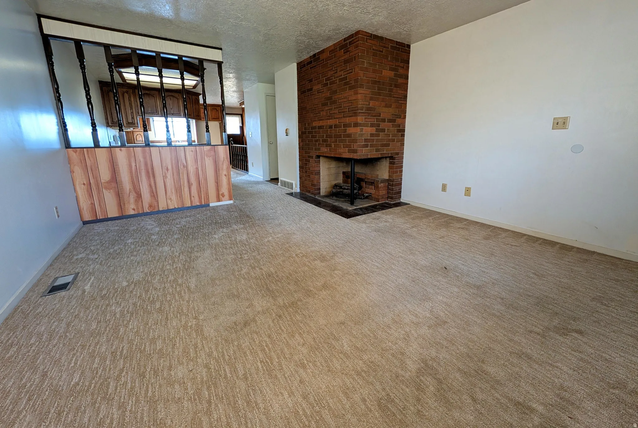 Unfurnished living room featuring a textured ceiling, a brick fireplace, and light carpet