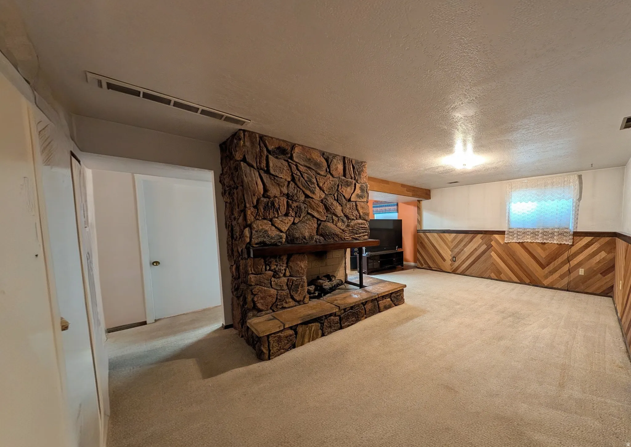 Stone fireplace with a wood mantel and hearth, wall-to-wall carpeting, wood-finish paneling, white walls, and a visible ceiling vent