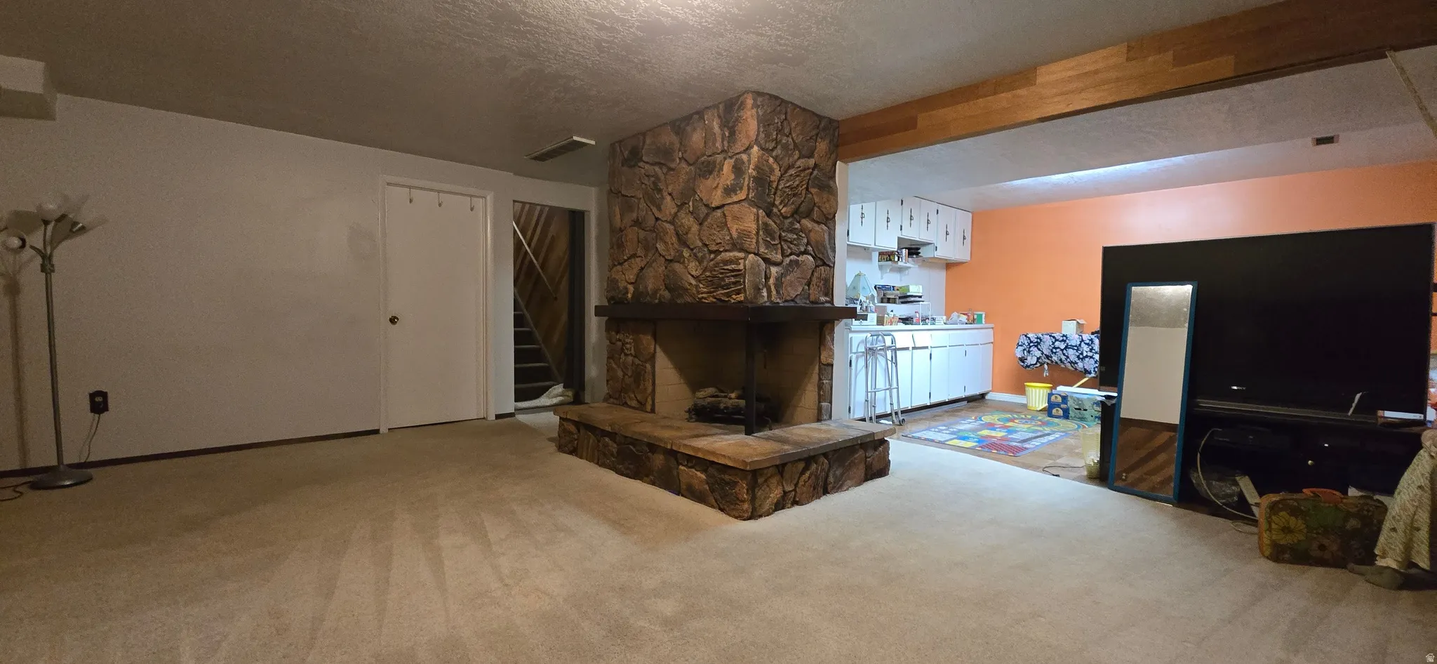 Carpeted living area featuring a stone fireplace, a textured ceiling, and stairway