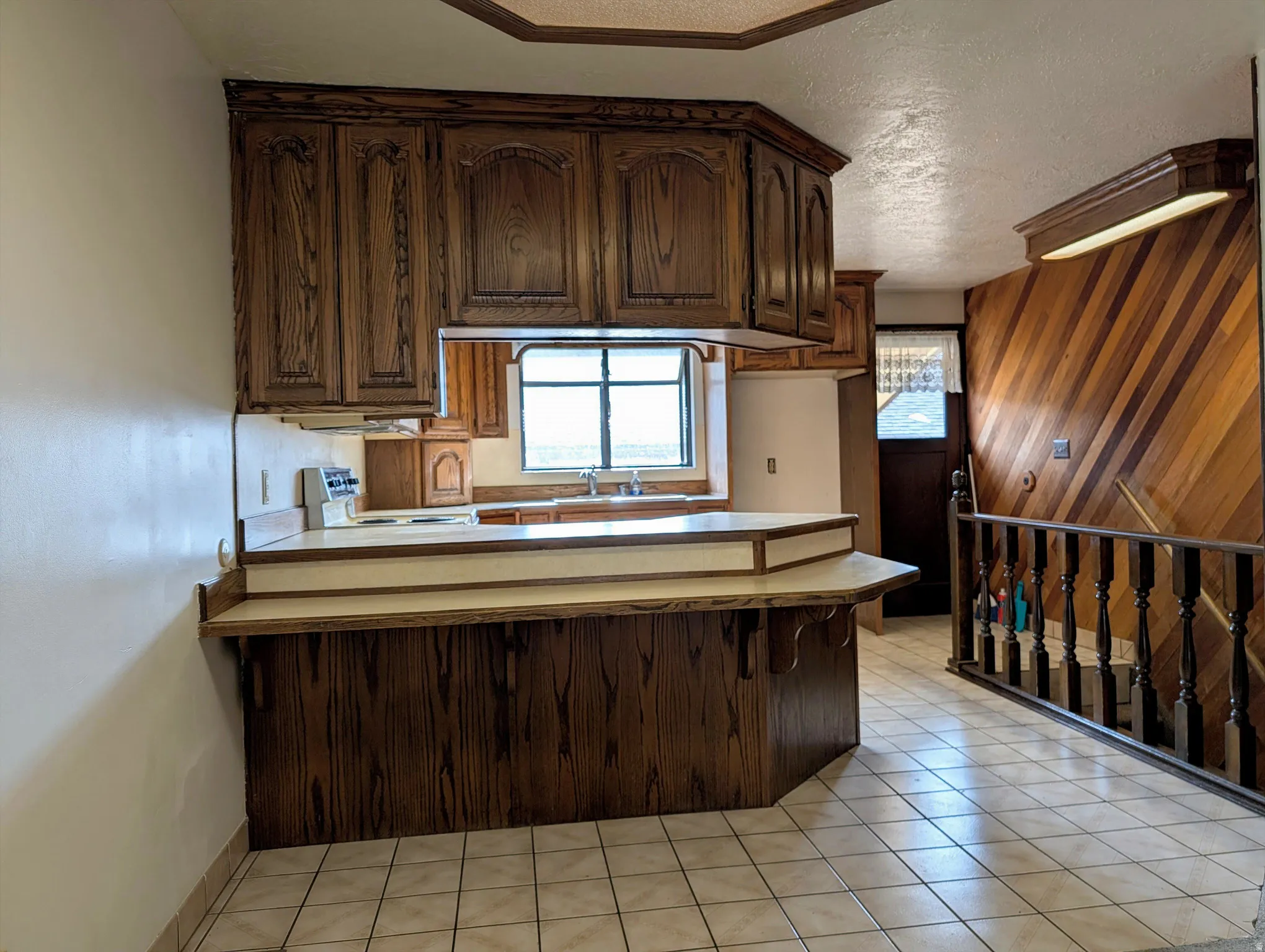 Kitchen featuring dark brown cabinets, a peninsula, light countertops, a textured ceiling, and stainless steel stove