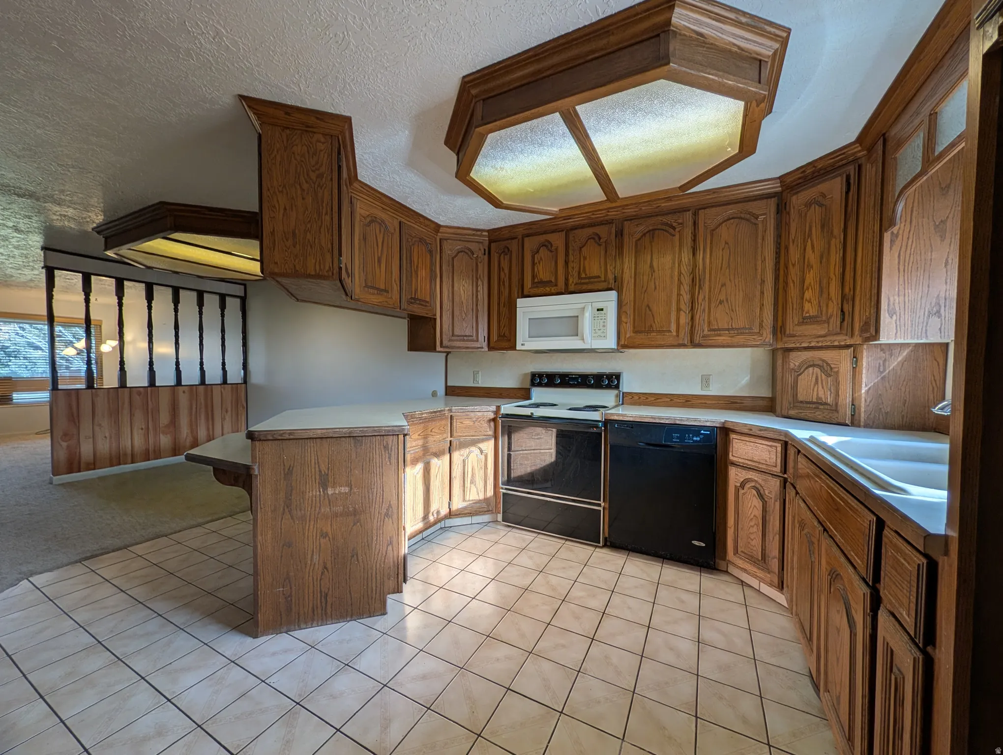 Kitchen featuring a peninsula, a kitchen breakfast bar, electric stove, dishwasher, and a textured ceiling