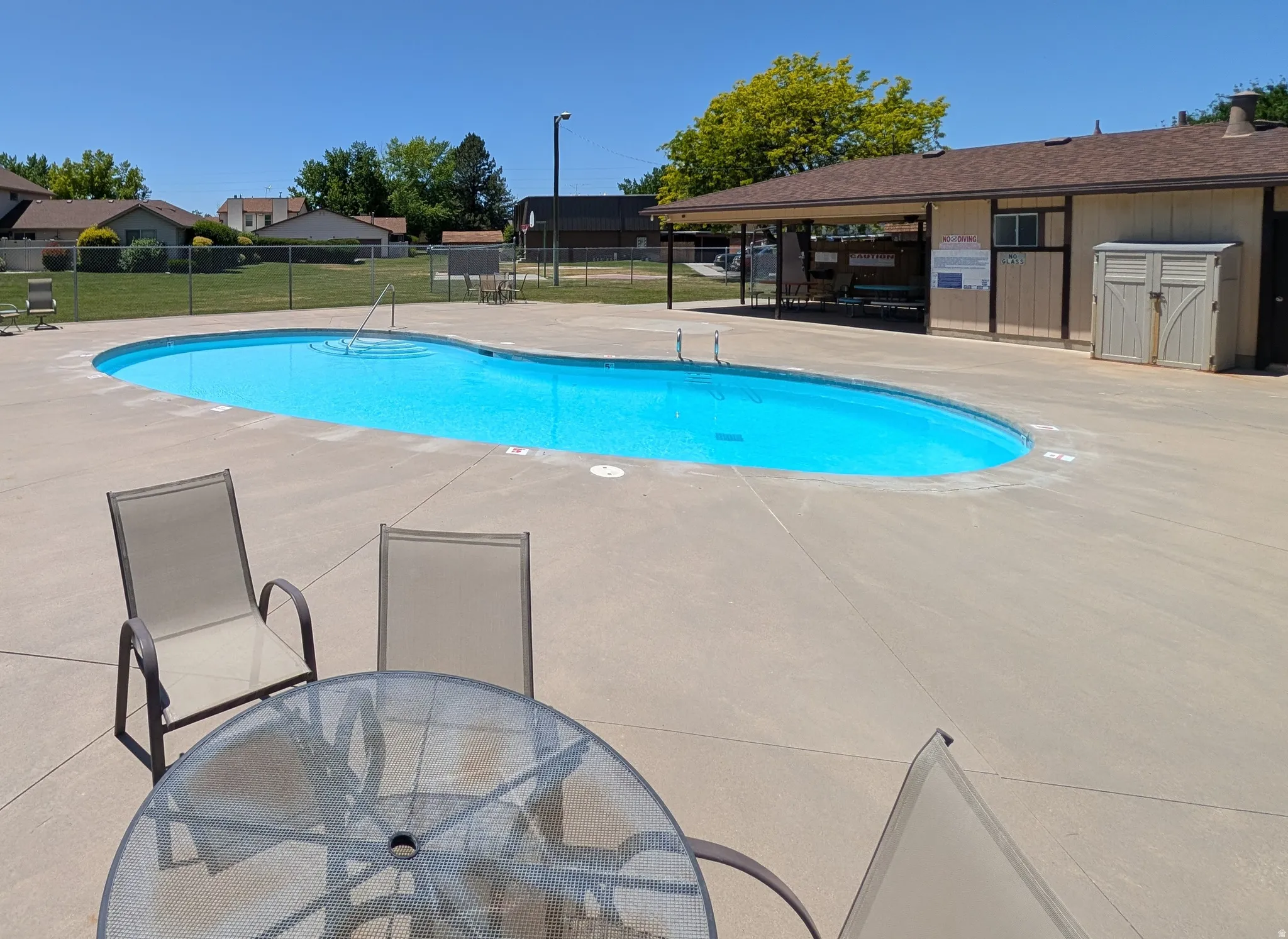 Resort-style pool area featuring a kidney-shaped pool, expansive concrete decking, covered patio structure, and a dedicated storage shed