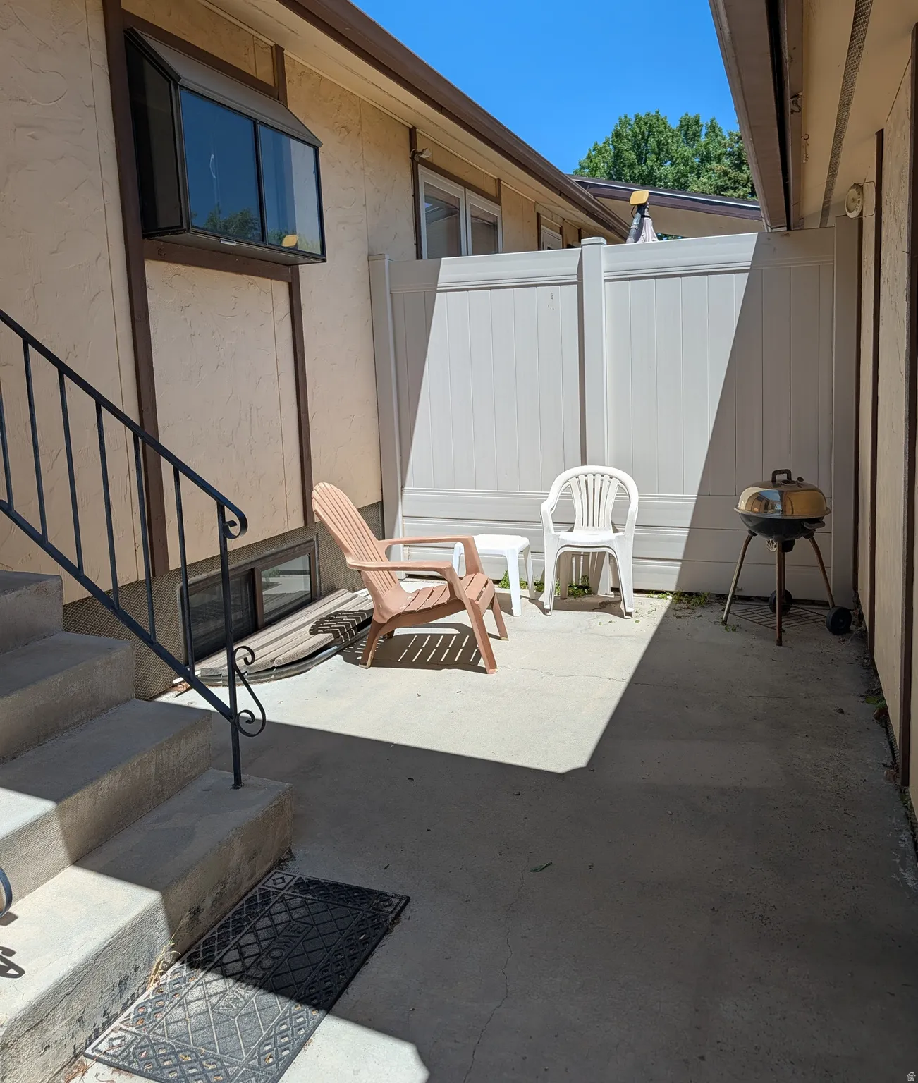 Private outdoor concrete patio area featuring a light-toned privacy fence and direct access to exterior stairs with a metal handrail