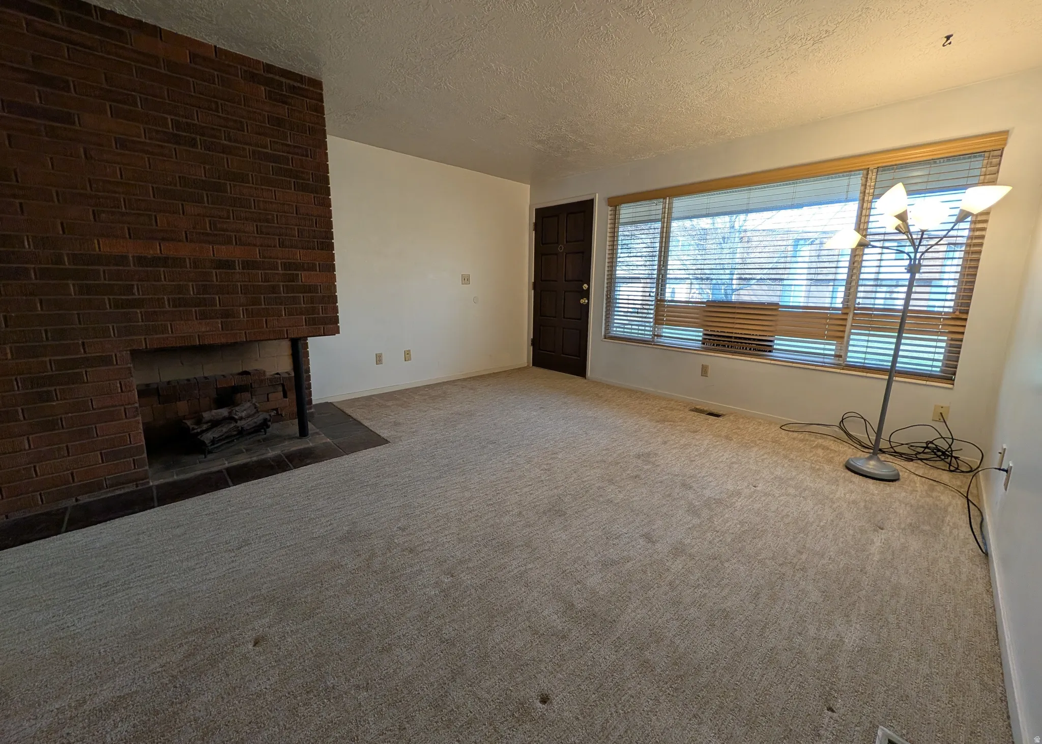Unfurnished living room featuring a textured ceiling, a fireplace, and carpet flooring