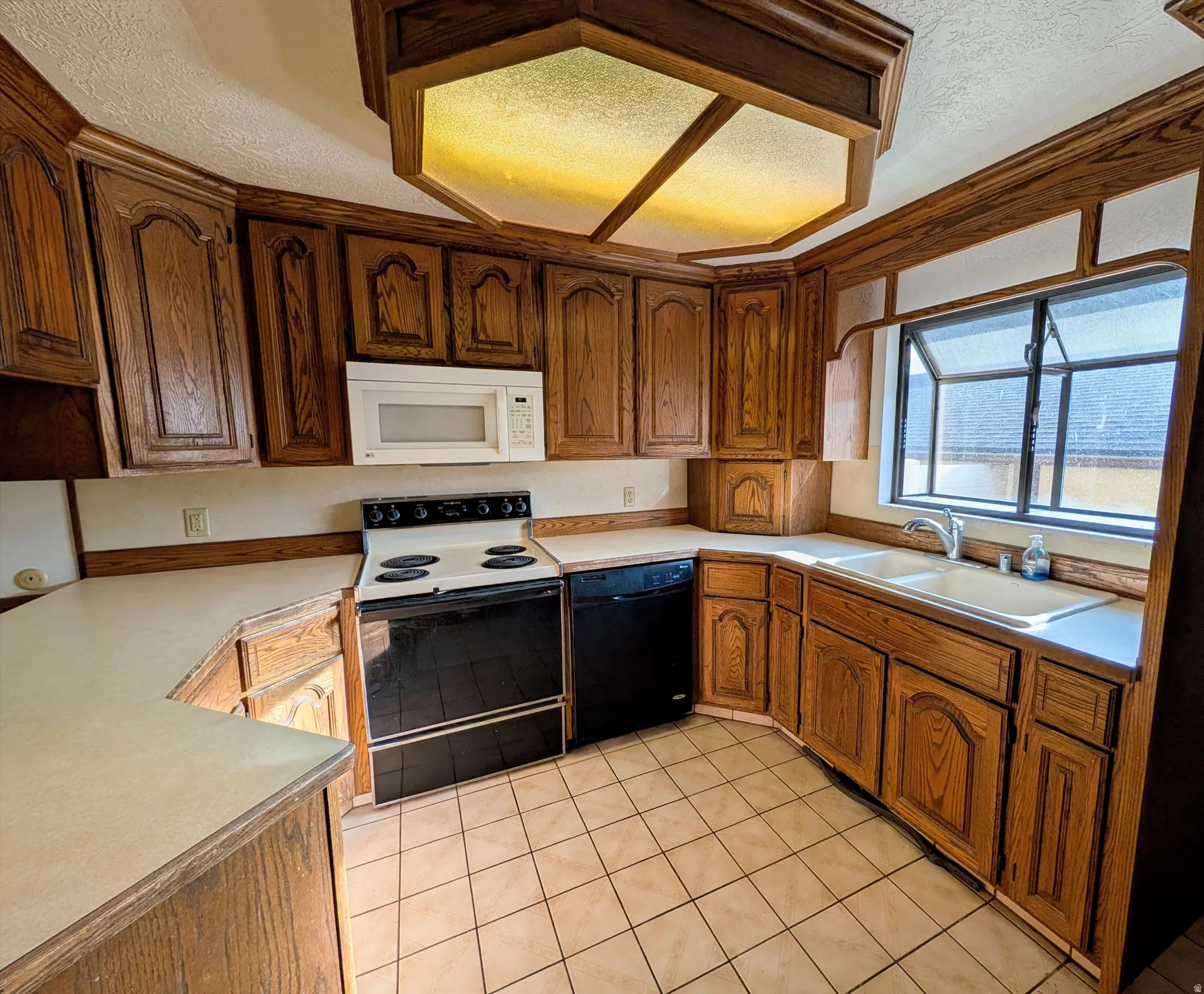 Kitchen featuring electric range, a textured ceiling, light countertops, black dishwasher, and white microwave
