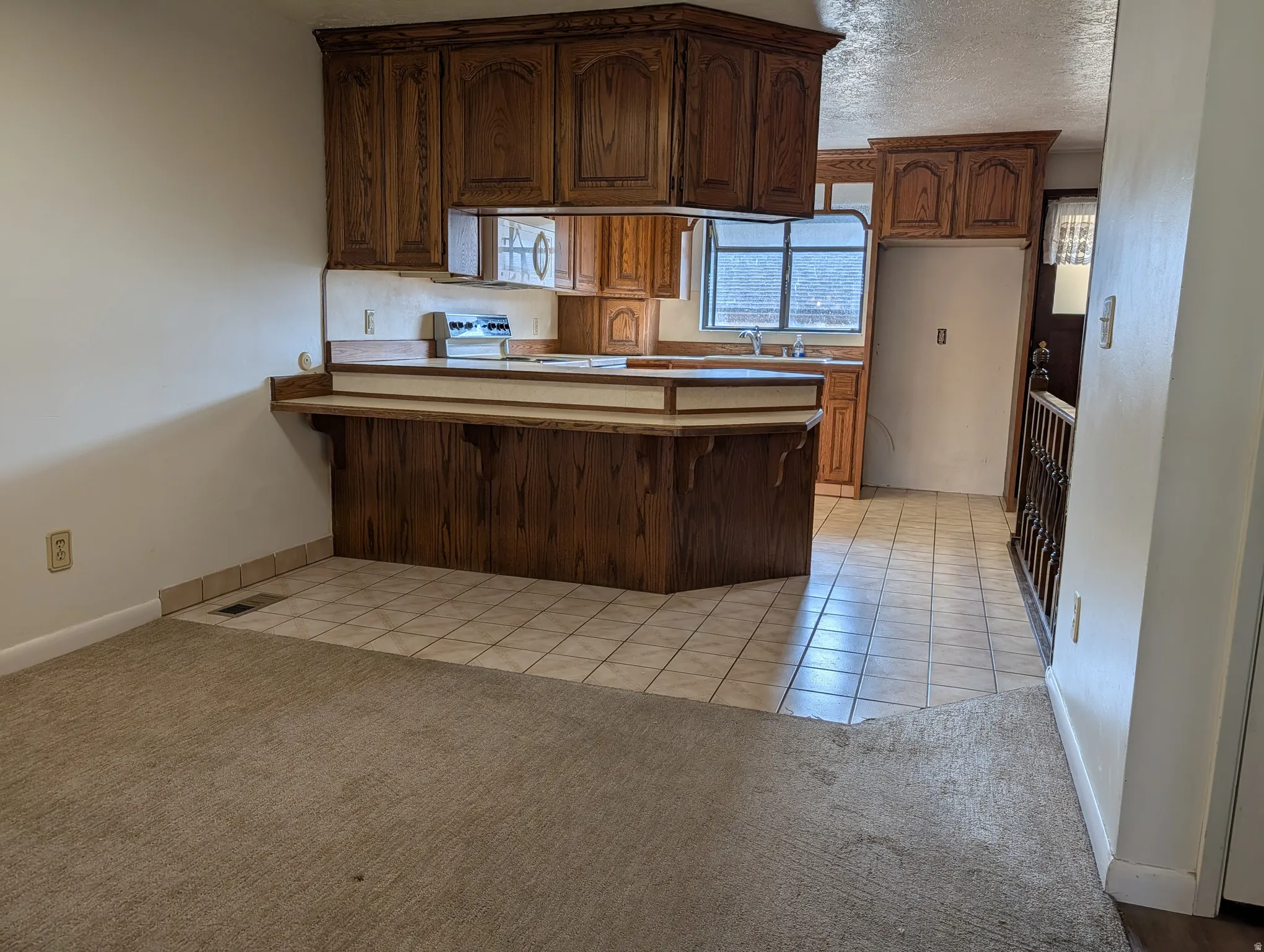 Kitchen featuring a peninsula, light tile patterned floors, electric range, light colored carpet, and a textured ceiling
