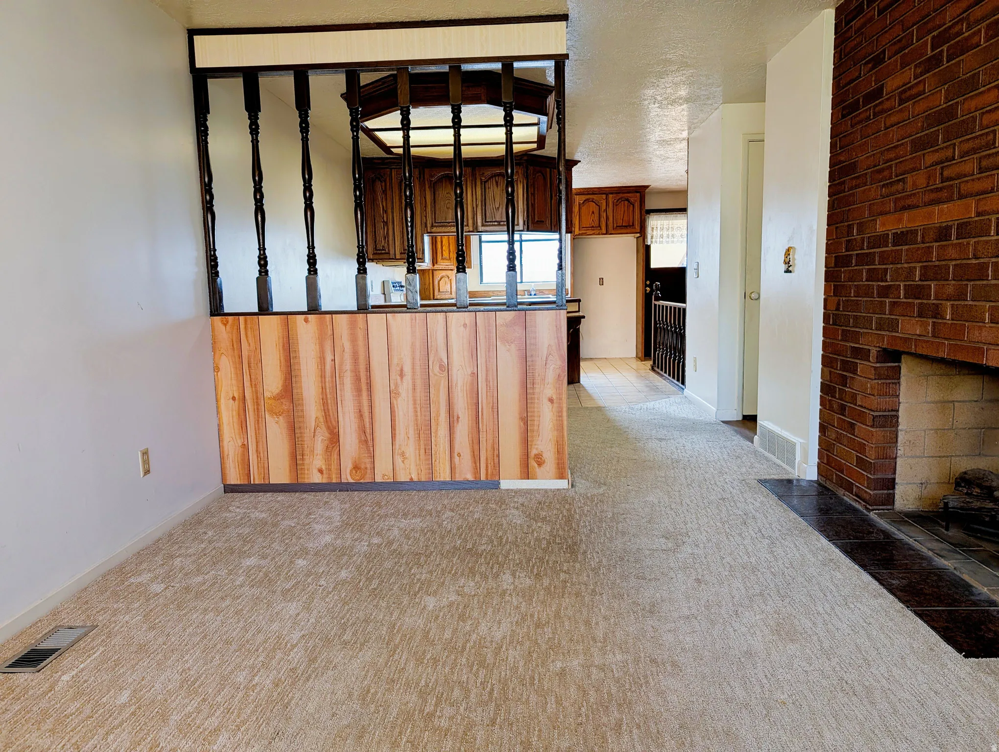 Kitchen featuring light colored carpet, a brick fireplace, a textured ceiling, a peninsula, and dark brown cabinets