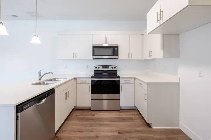 Modern kitchen with white cabinetry, stainless steel appliances, light-toned countertops, wood-finish flooring, and pendant lighting