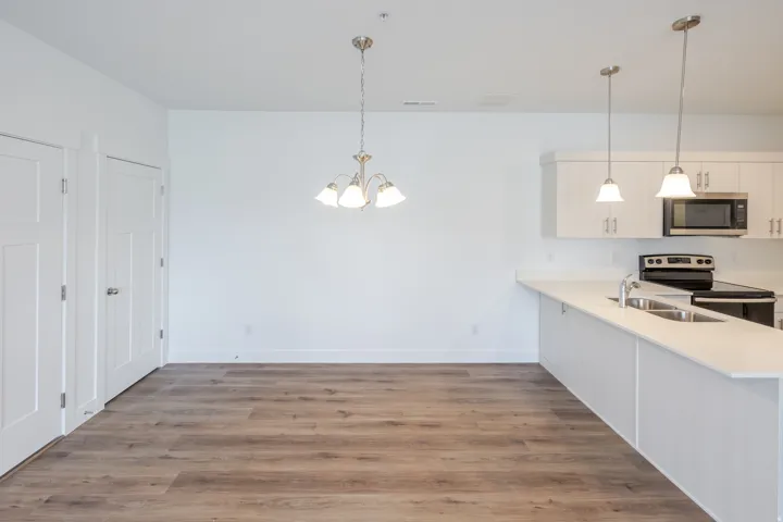 Open-concept living space featuring wood-finish flooring, white walls, and a contemporary kitchen with white cabinetry and light-colored countertops