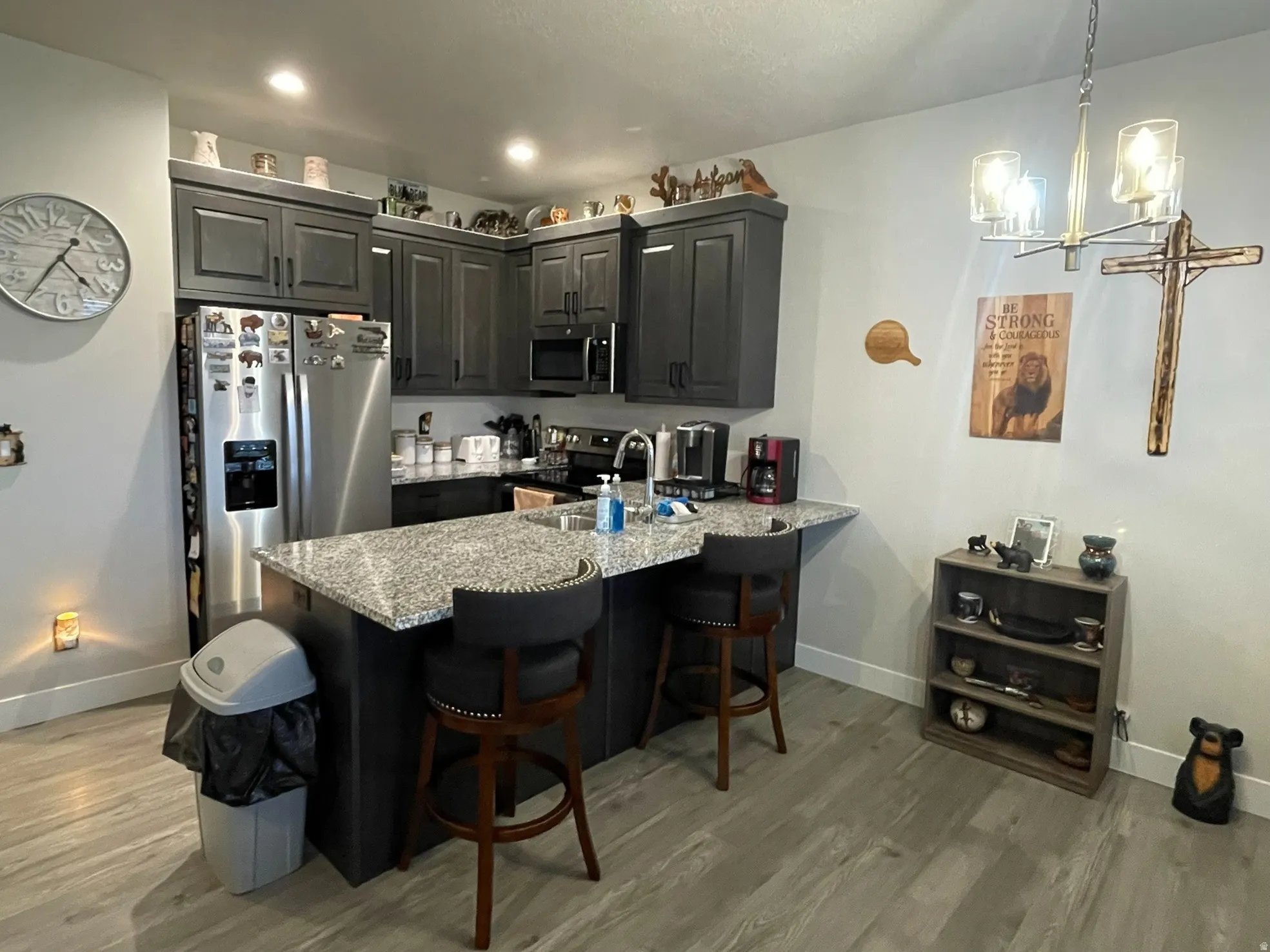 Kitchen with lvp flooring, stainless steel appliances, a breakfast bar, a chandelier, granite countertops.