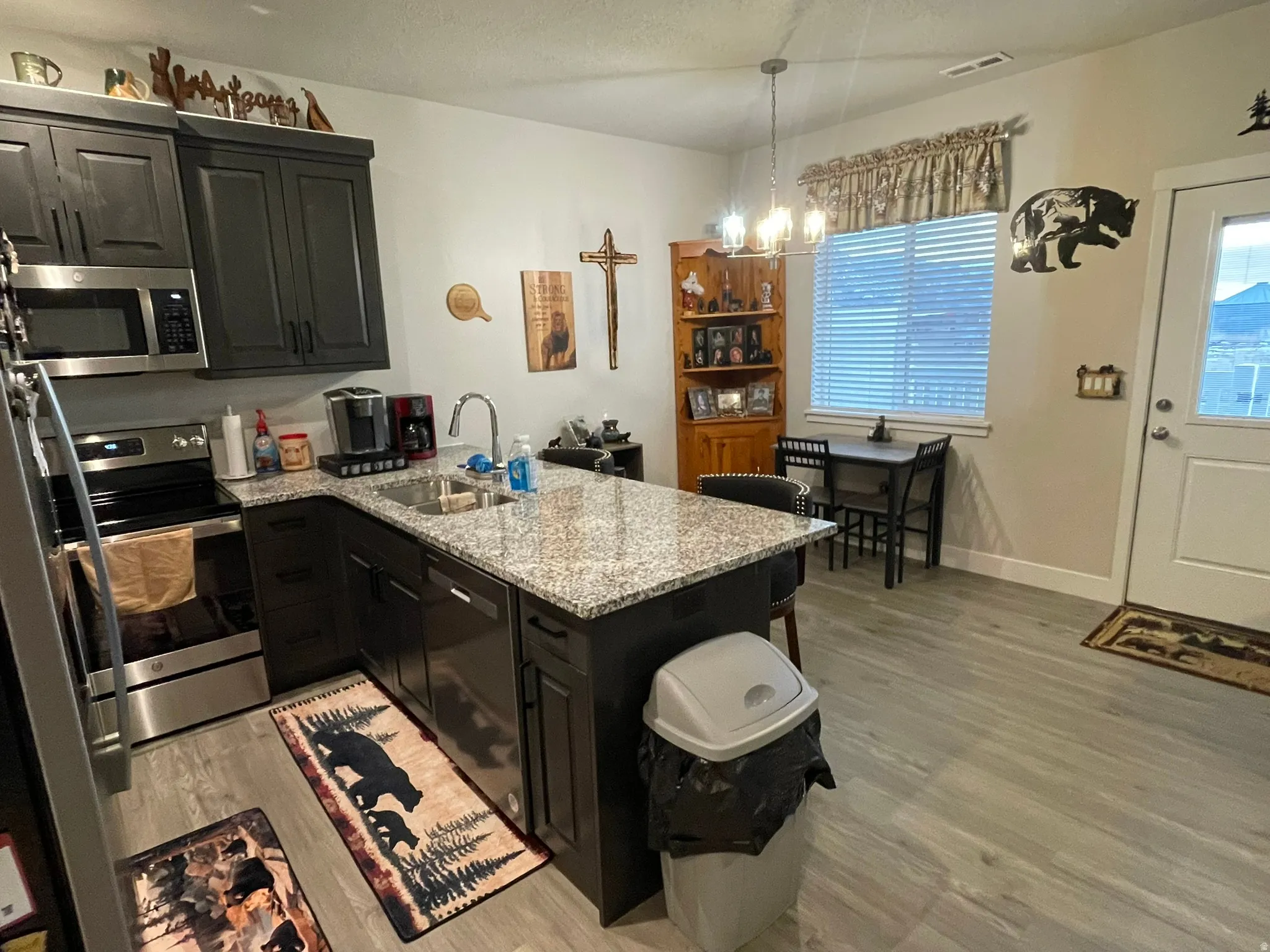 Kitchen featuring stainless steel appliances, granite countertops, lvp flooring, peninsula, and dark cabinets