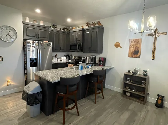 Kitchen with lvp flooring, stainless steel appliances, a breakfast bar, a chandelier, granite countertops.