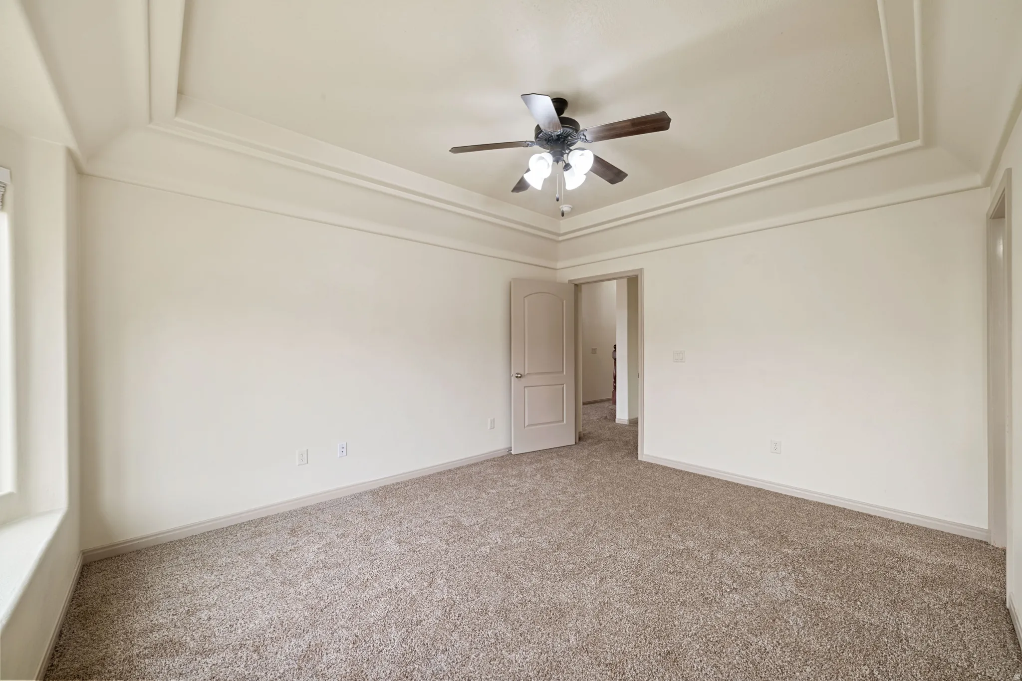 Carpeted empty room with a raised ceiling and ceiling fan