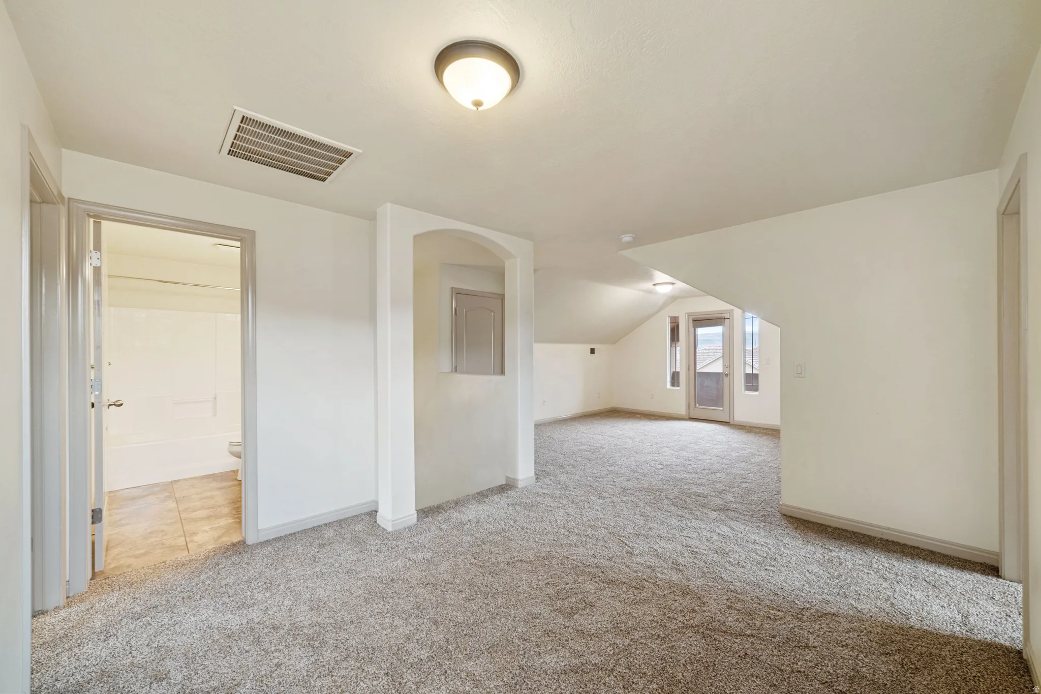 Additional living space with light carpet and vaulted ceiling