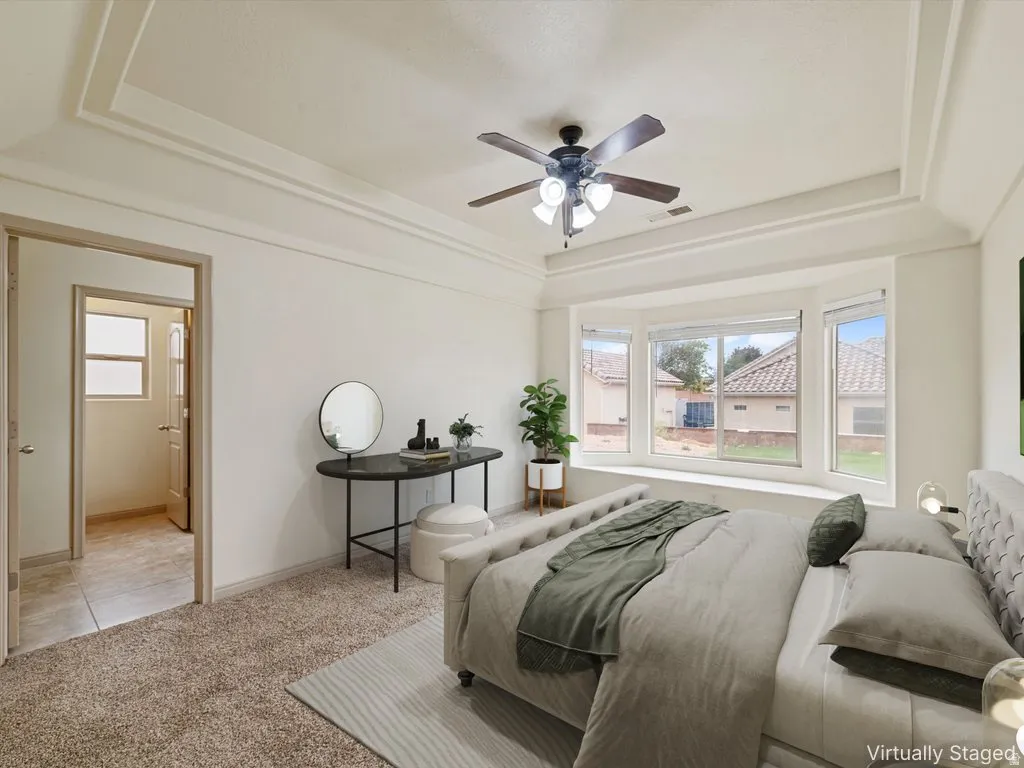 Bedroom with a tray ceiling, light colored carpet, a ceiling fan, and connected bathroom
