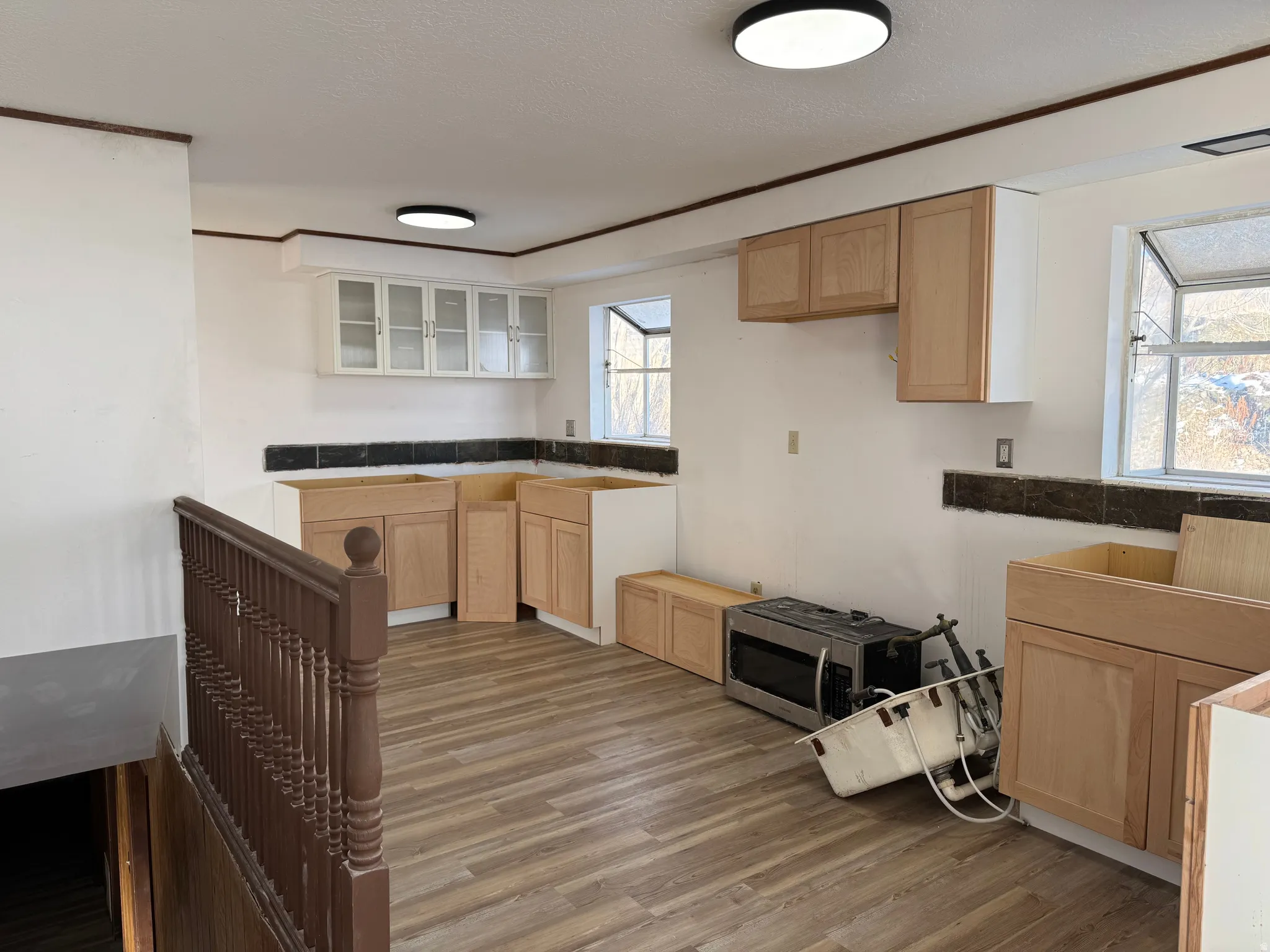 Kitchen featuring light brown cabinetry, stainless steel microwave, dark wood finished floors, glass insert cabinets, and a textured ceiling