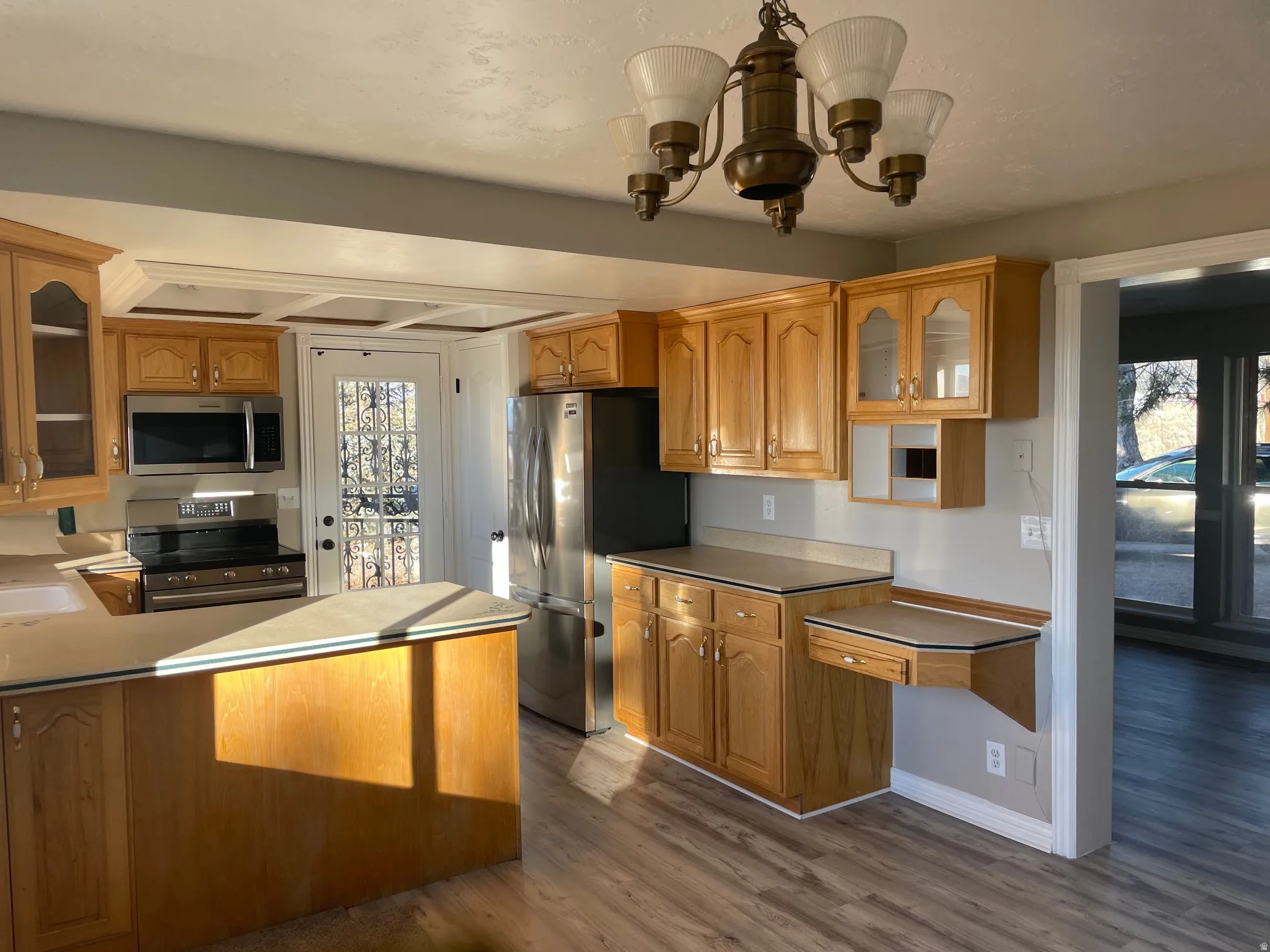 Kitchen featuring glass insert cabinets, stainless steel appliances, dark wood-style floors, and brown cabinetry