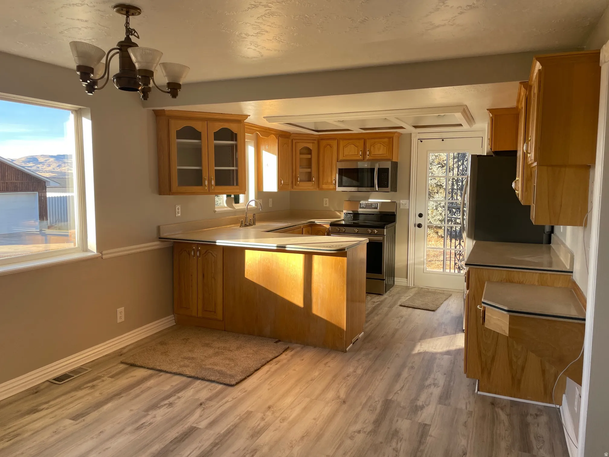 Kitchen featuring glass insert cabinets, appliances with stainless steel finishes, light countertops, a peninsula, and light wood-style flooring
