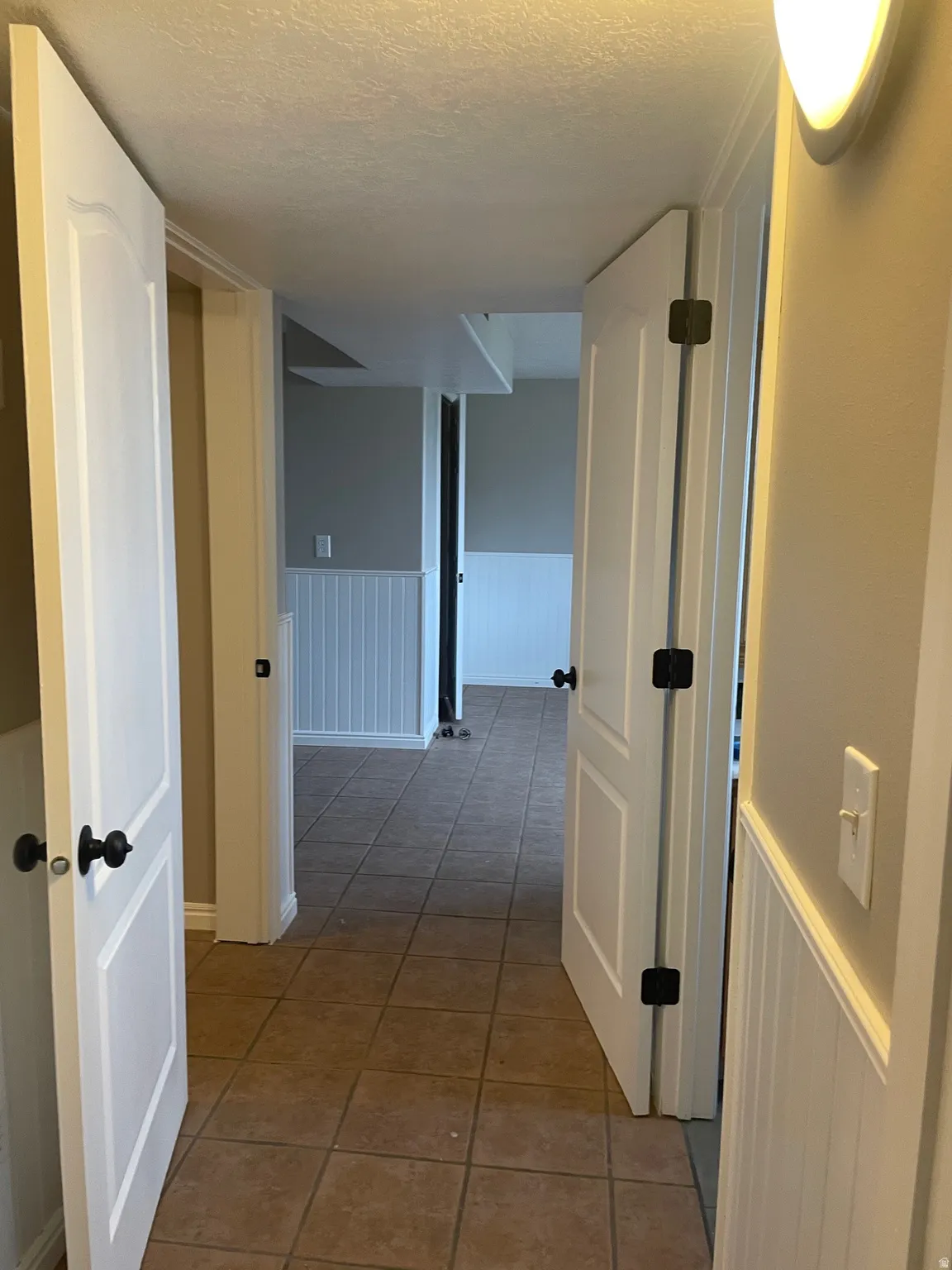 Corridor with wainscoting, light tile patterned floors, and a textured ceiling